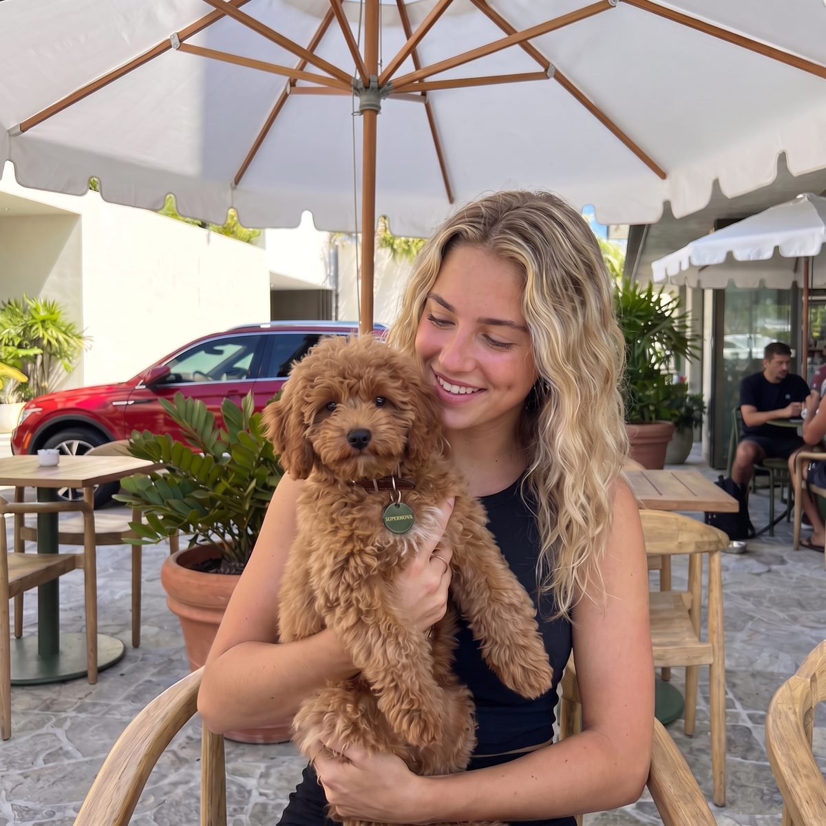 Smiling owner at a café holding her red cockapoo puppy, a PawTag on its collar